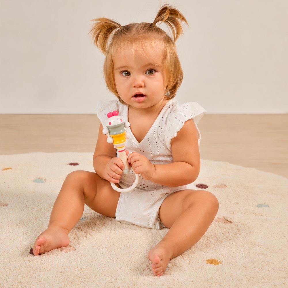 Miniland - Chick bell – bambina che tiene in mano il sonaglio seduta sul tappeto