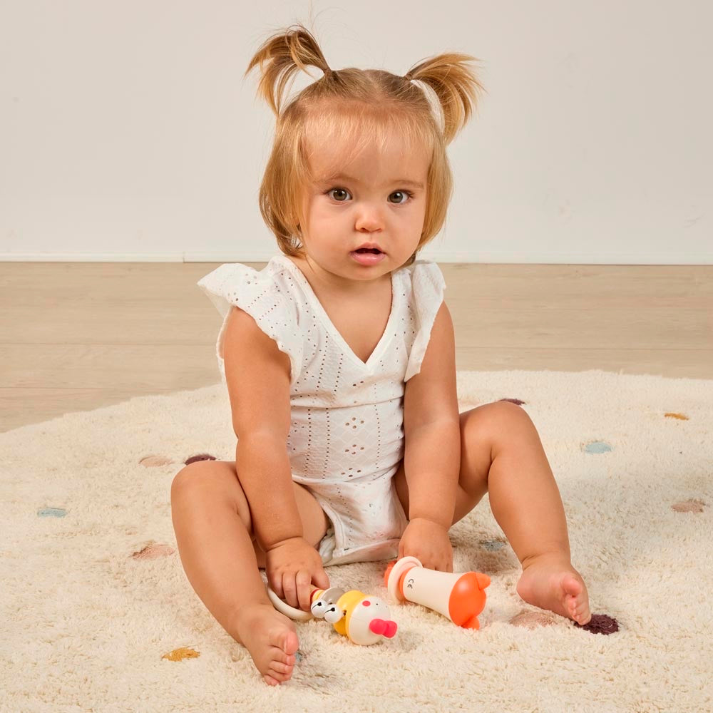 Miniland - Chick bell – bambina seduta sul tappeto con il sonaglio e un altro sonaglio Miniland