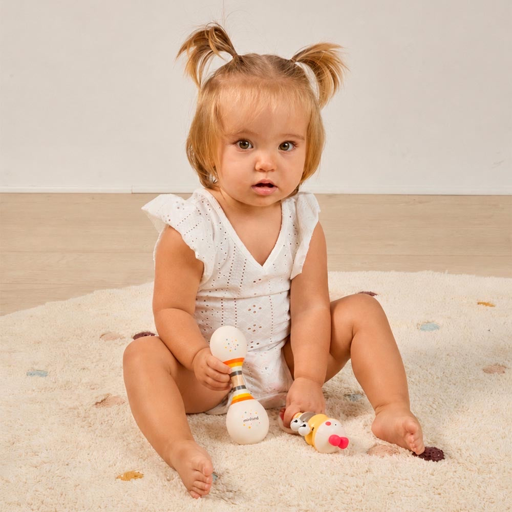 Miniland - Soft duo rattle – bambina seduta sul tappeto con il sonaglio e il Chick bell