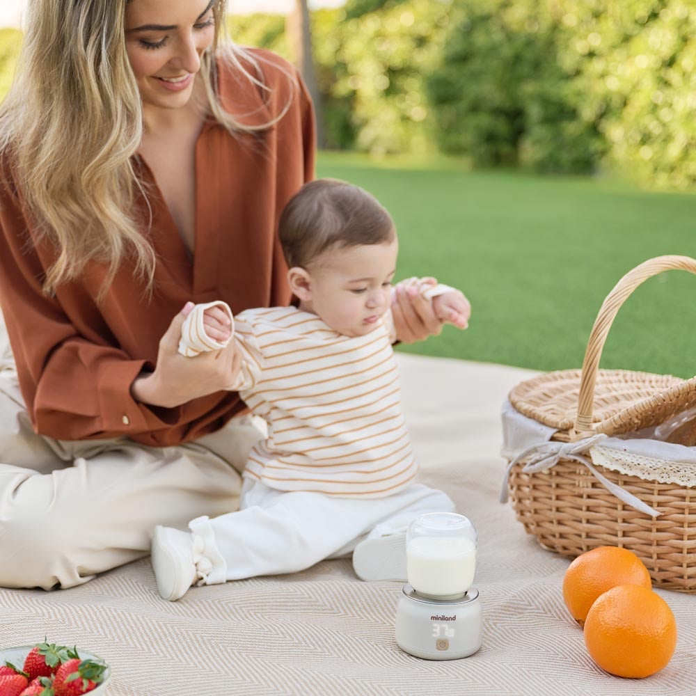 Miniland - Scaldabiberon portatile Warmy on the Go Plus – mamma con il bebè durante un picnic con lo scaldabiberon
